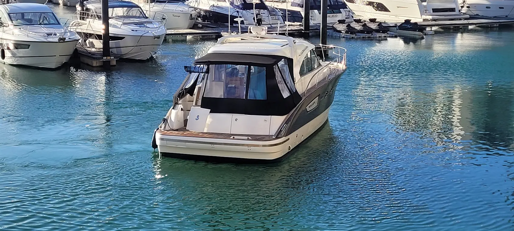 A sleek motorboat docks in clear blue water, surrounded by various other boats at a marina.